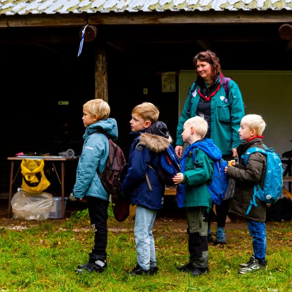 To spejderledere viser en færdselstavle for en gruppe børn